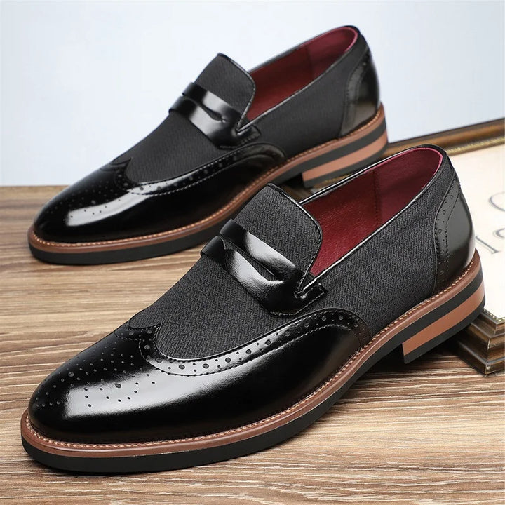 Black leather loafers with brown soles on a wooden surface