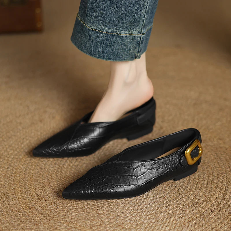 Black pointed-toe shoes with a gold buckle on a textured surface