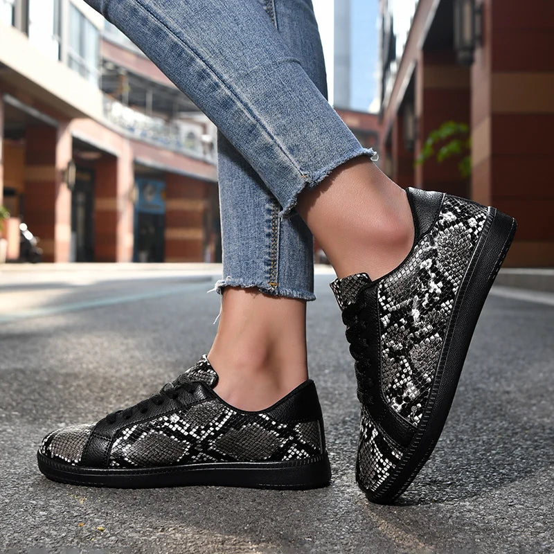 Black and silver patterned sneakers worn with blue jeans on a street.