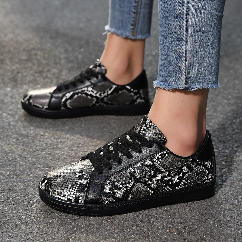 Black and silver patterned sneakers worn with jeans on a gray pavement.