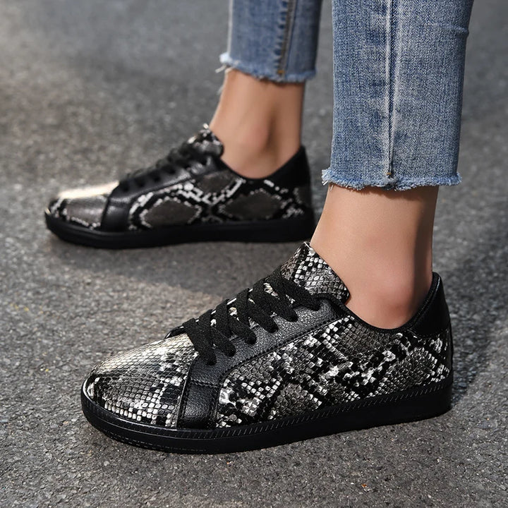 Black and silver patterned sneakers worn with jeans on a gray pavement.