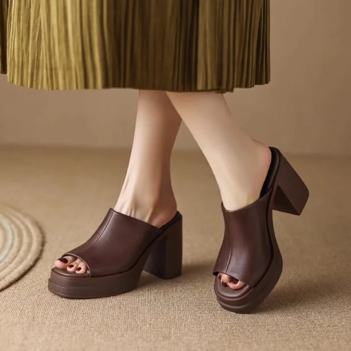 Brown platform sandals worn with a pleated skirt on a beige background