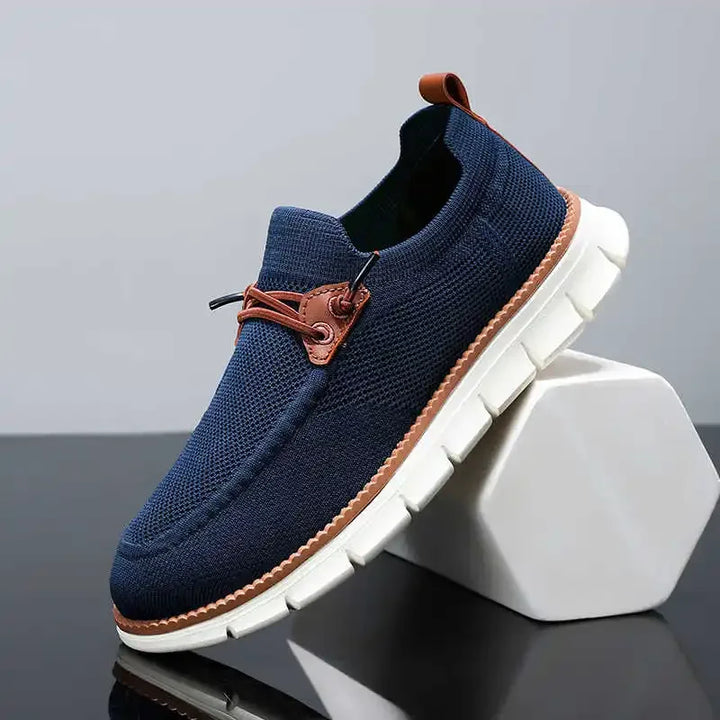 Navy blue slip-on shoe with brown accents on a gray background