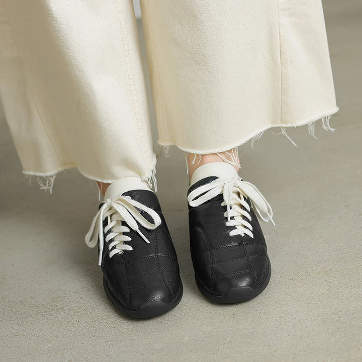 Black sneakers with white laces worn with light-colored pants on a neutral background
