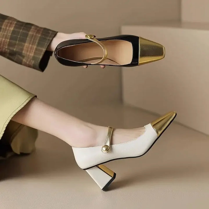White and gold high-heeled shoes worn by a person sitting on a beige surface.