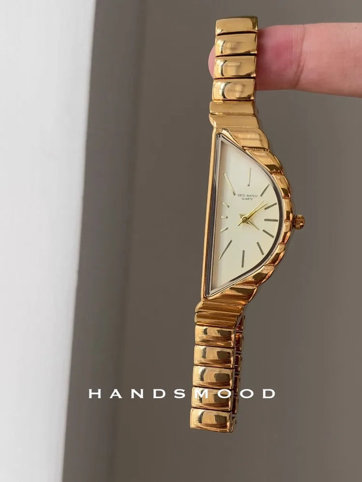 Gold wristwatch held by a finger against a neutral background, with 'HANDSWOOD' branding.