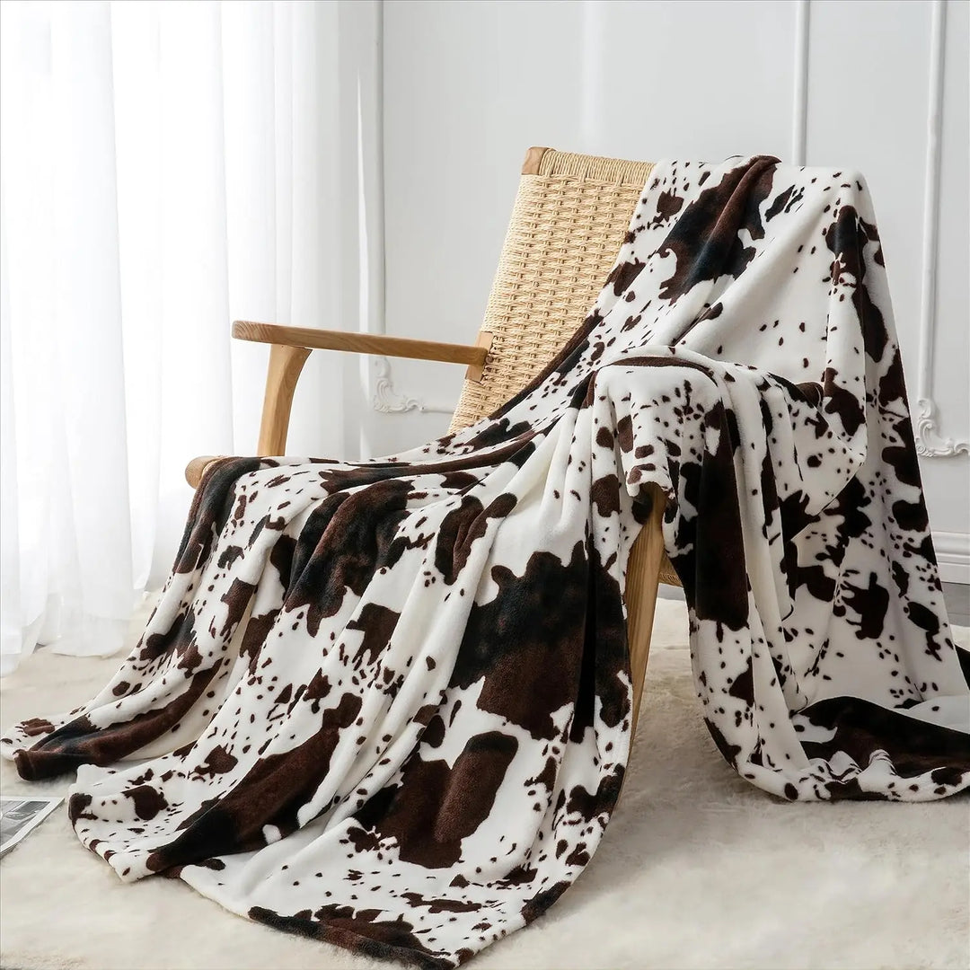 Cow print blanket draped over a wooden chair in a room with white curtains.