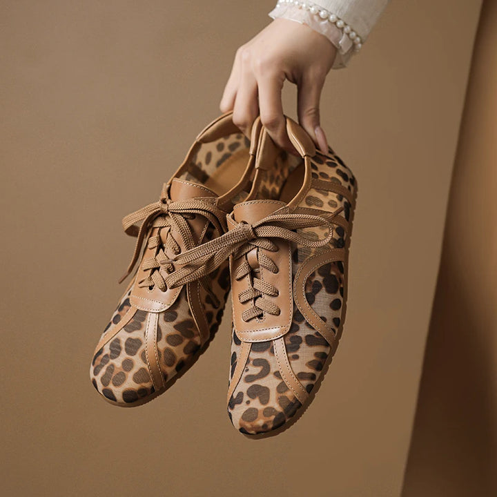 Pair of leopard print shoes held by a hand against a beige background