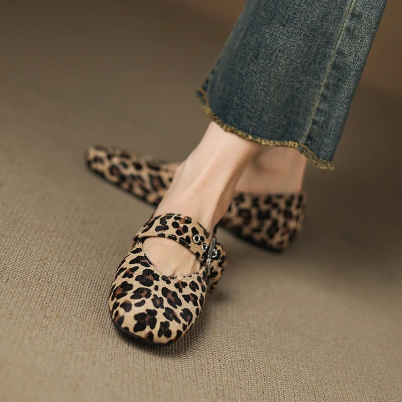 Leopard print flats worn with jeans on a beige surface