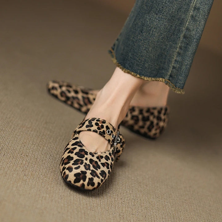 Leopard print flats worn with jeans on a beige surface
