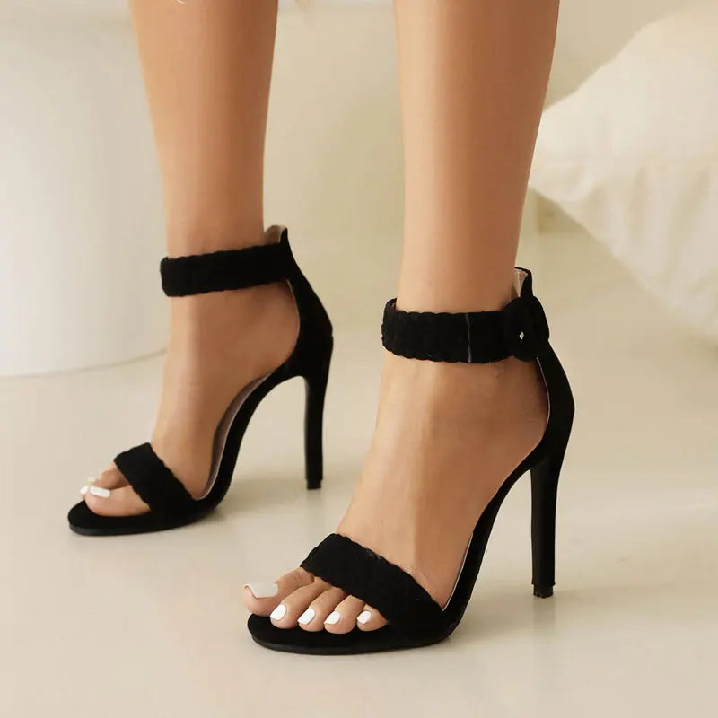 Black high-heeled sandals worn by a person on a neutral background