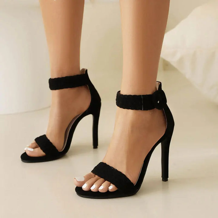 Black high-heeled sandals worn by a person on a neutral background