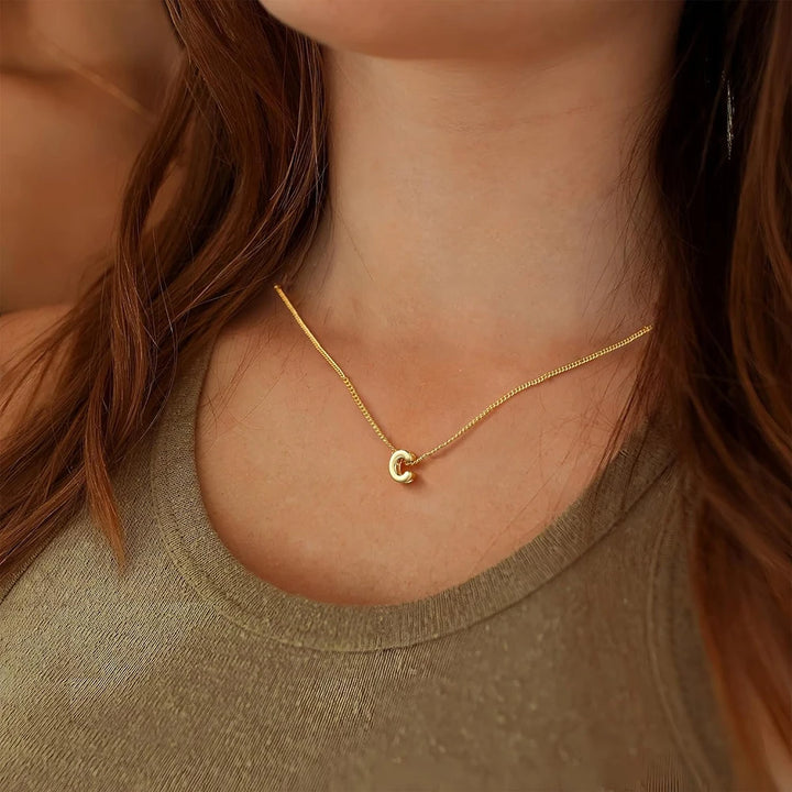 Gold necklace with a small round pendant worn by a person with brown hair.