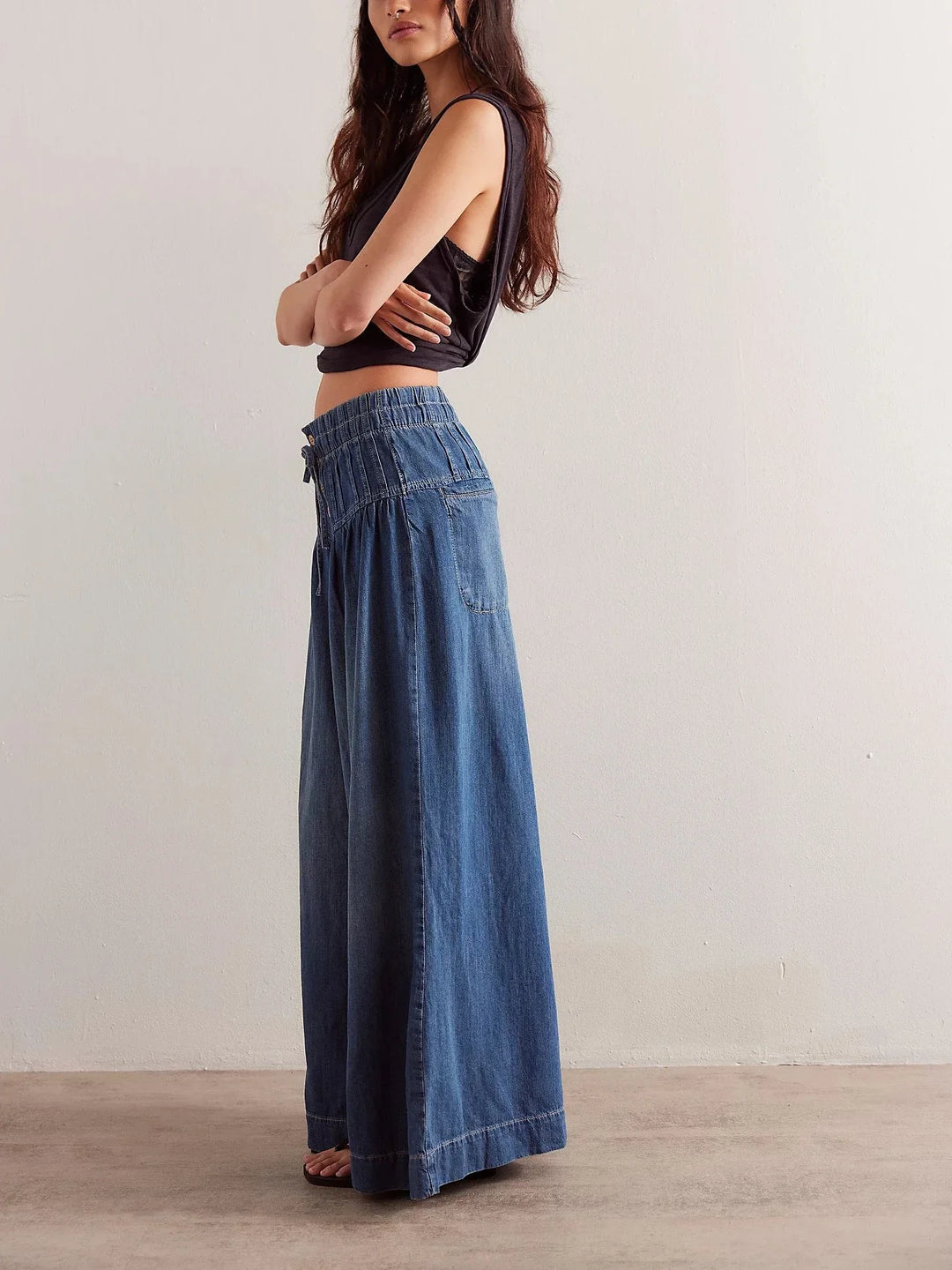 Woman wearing a black crop top and blue denim wide-leg pants against a plain background
