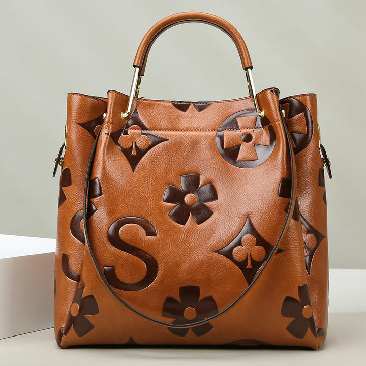Brown leather handbag with floral patterns on a light background