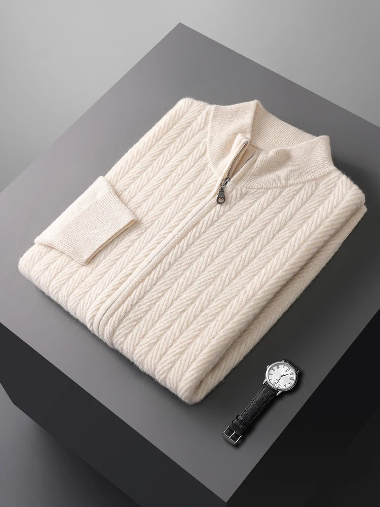 Folded cream-colored cable knit sweater on a dark surface with a watch beside it