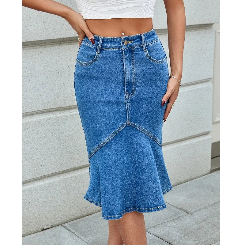 Person wearing a blue denim skirt with a white top against a stone wall.