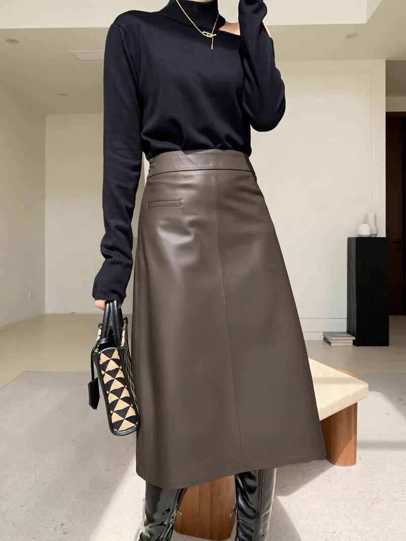 Person wearing a black long-sleeve top and brown leather skirt holding a patterned handbag indoors.