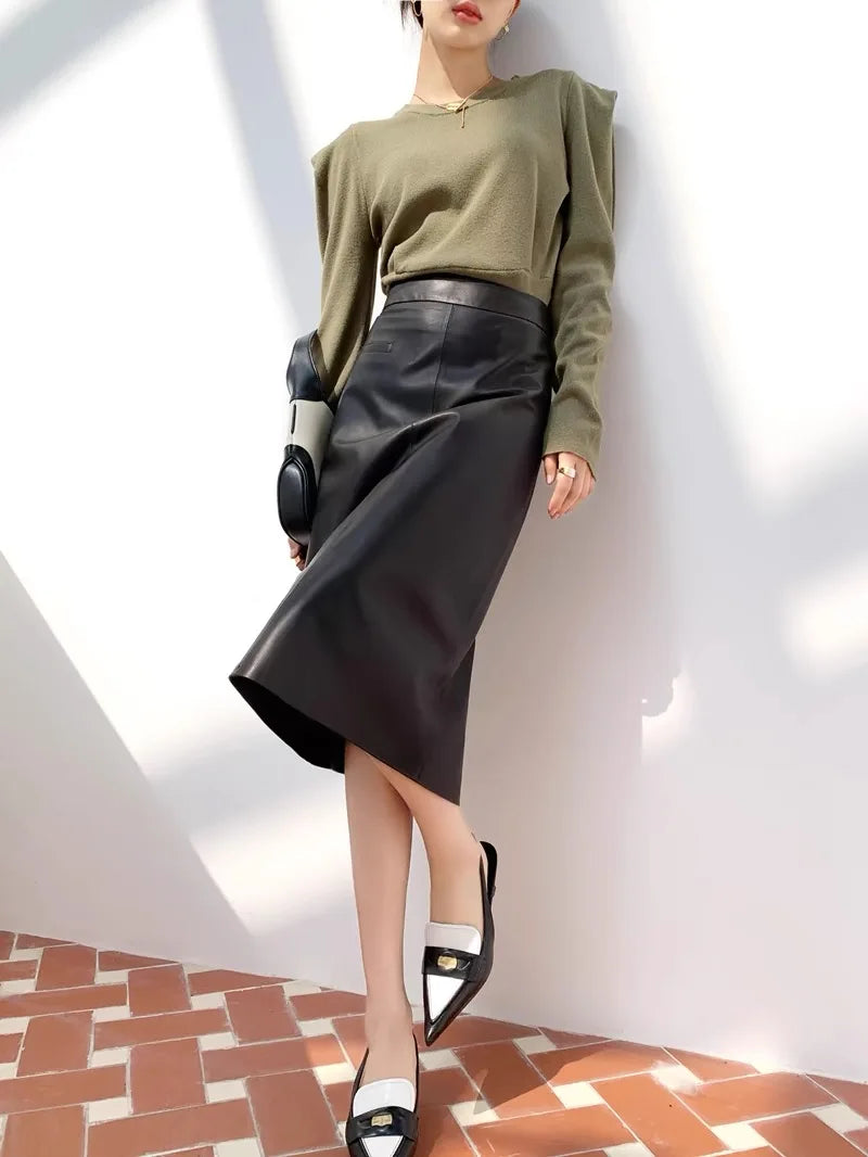 Person wearing a green sweater and black leather skirt in a minimalistic setting