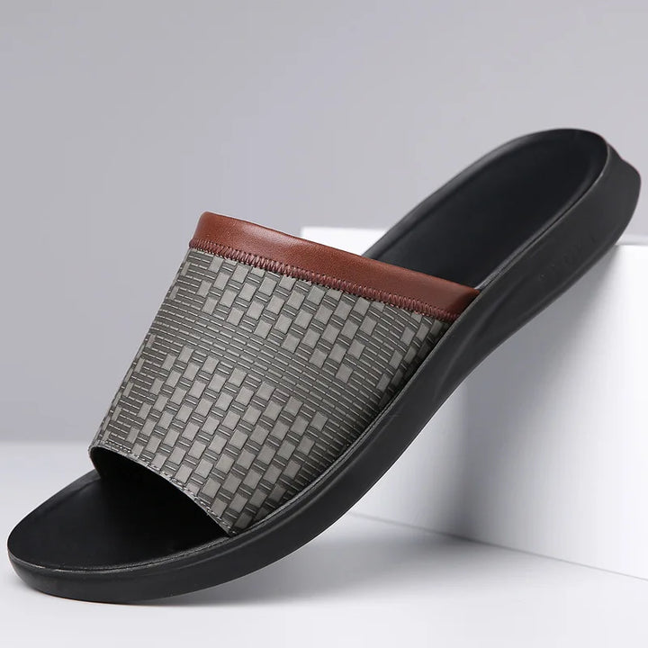 Gray slide sandal with brown woven strap on a white background