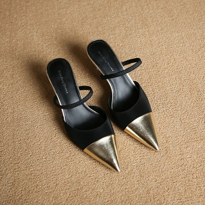 Black high-heeled shoes with gold tips on a beige surface