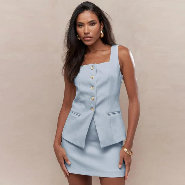 Woman wearing a light blue dress with gold buttons against a beige background