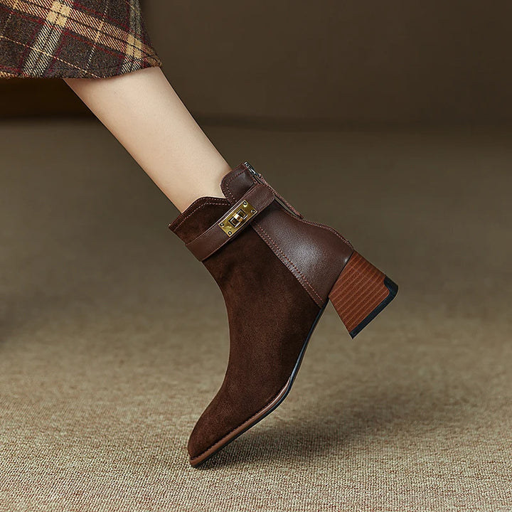 Brown suede ankle boot with a gold buckle on a textured brown surface