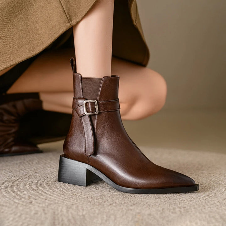 Brown leather boot with a buckle on a neutral background