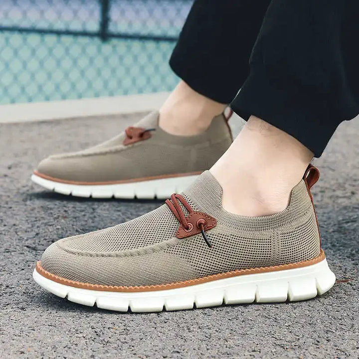 Brown casual shoes with white soles worn by a person on a textured surface.