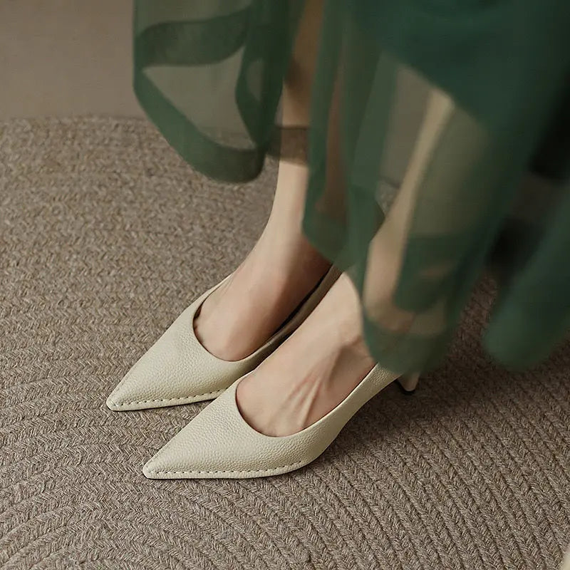 White pointed-toe shoes worn with green pants on a textured surface