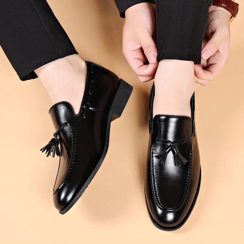 Black leather shoes with tassels worn by a person on a beige background