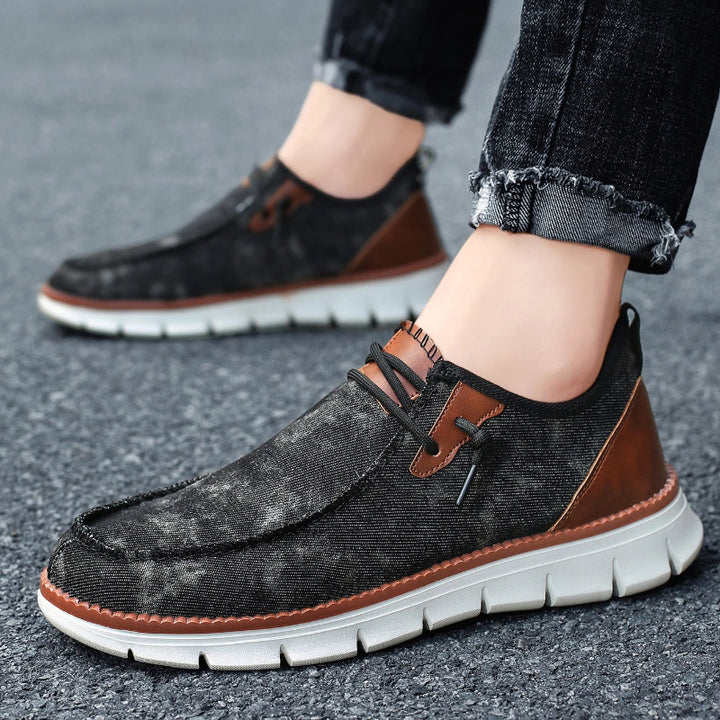 Black and brown casual shoes worn with rolled-up jeans on a blurred street background