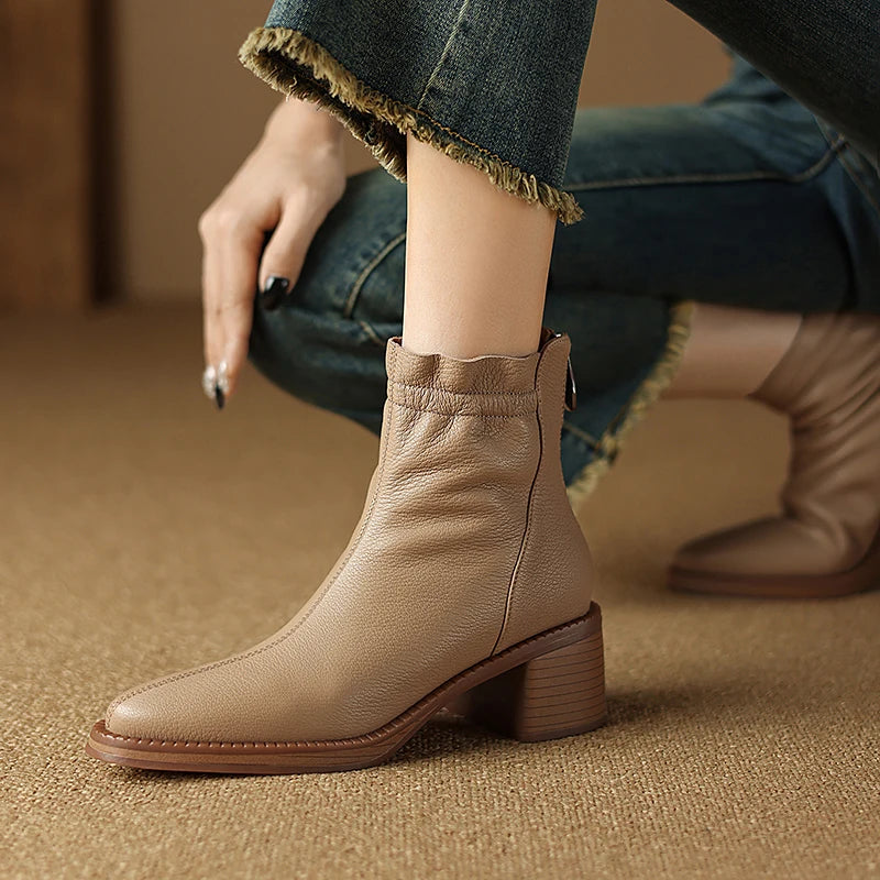 Beige ankle boots worn with rolled-up jeans on a textured surface