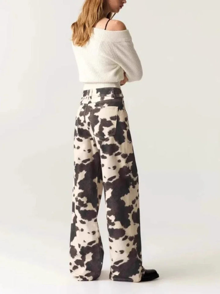 Person wearing a white off-shoulder top and cow print pants on a white background