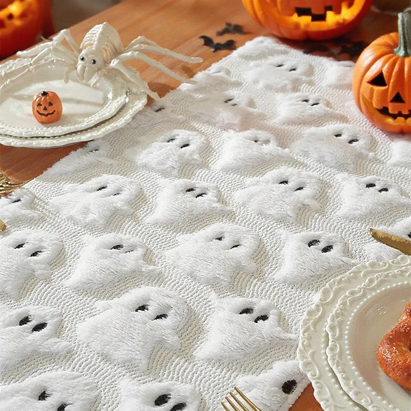 Halloween-themed tablecloth with ghost designs on a wooden table with pumpkins and spider decorations.