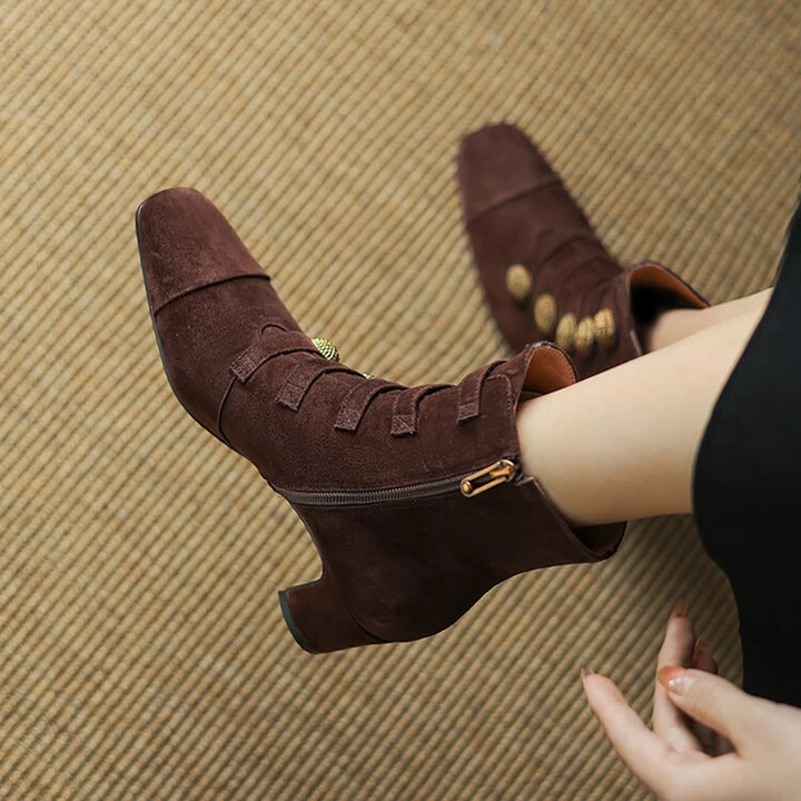 Brown suede boots with gold accents worn by a person on a textured brown surface