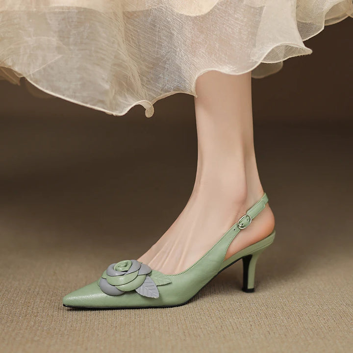 Green high-heeled shoes with floral design worn by a person in a light dress.