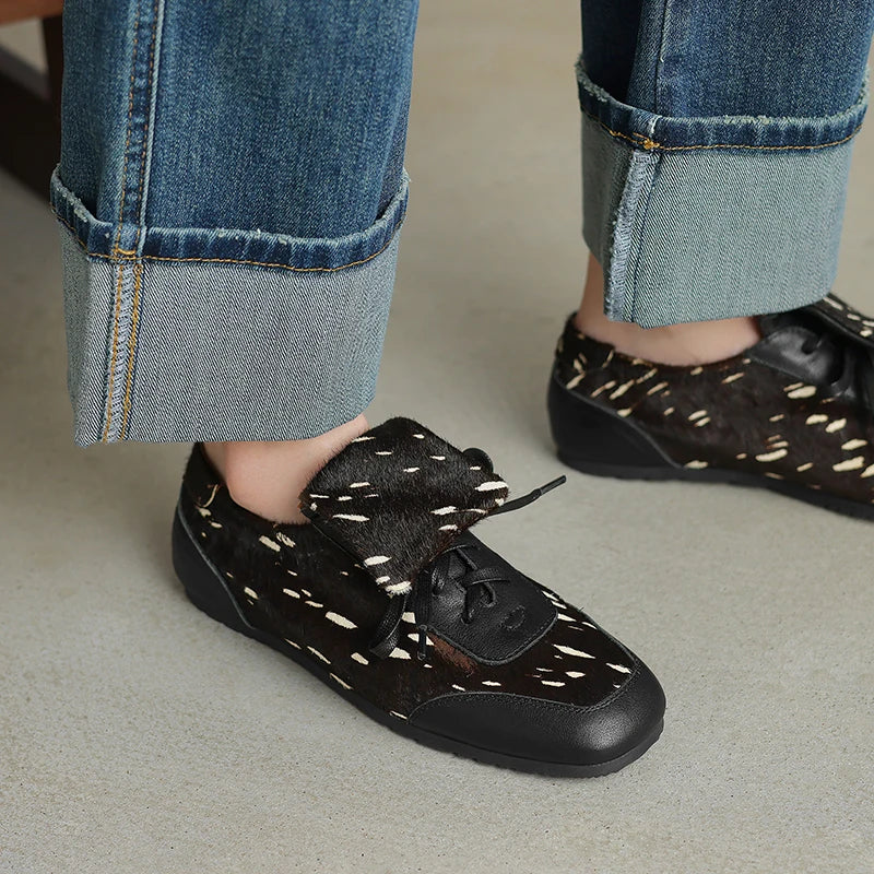 Black loafers with white patterns worn with rolled-up jeans on a neutral background