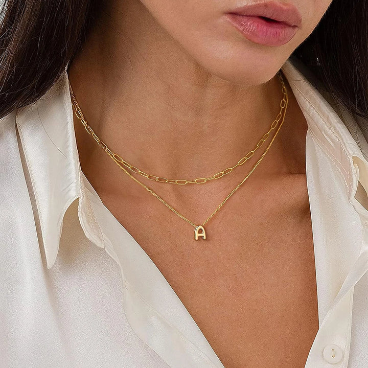 Gold chain necklace with a letter 'A' pendant worn by a person in a white shirt.