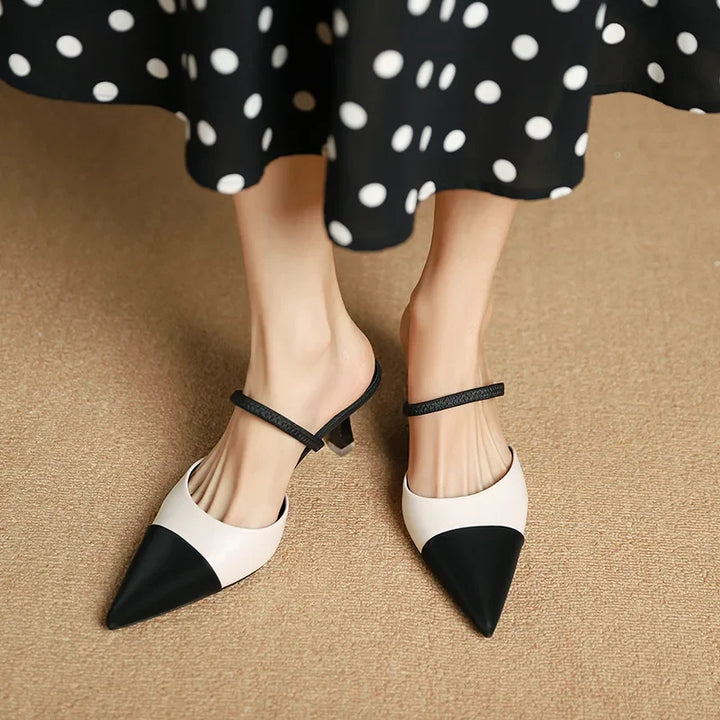 Black and white pointed-toe shoes worn with a polka dot skirt on a beige surface