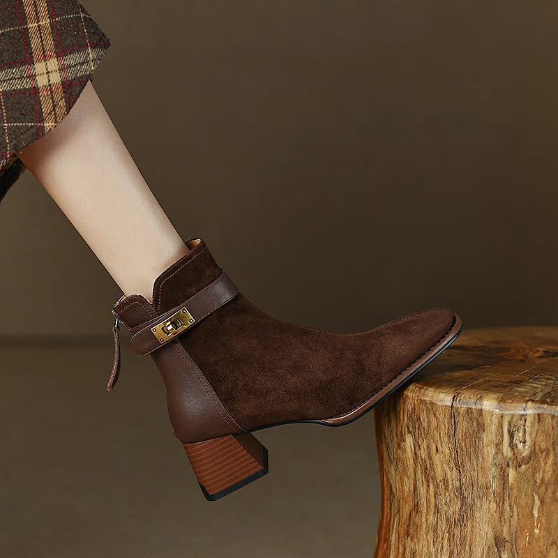 Brown suede ankle boots with a gold buckle on a wooden stool against a brown background