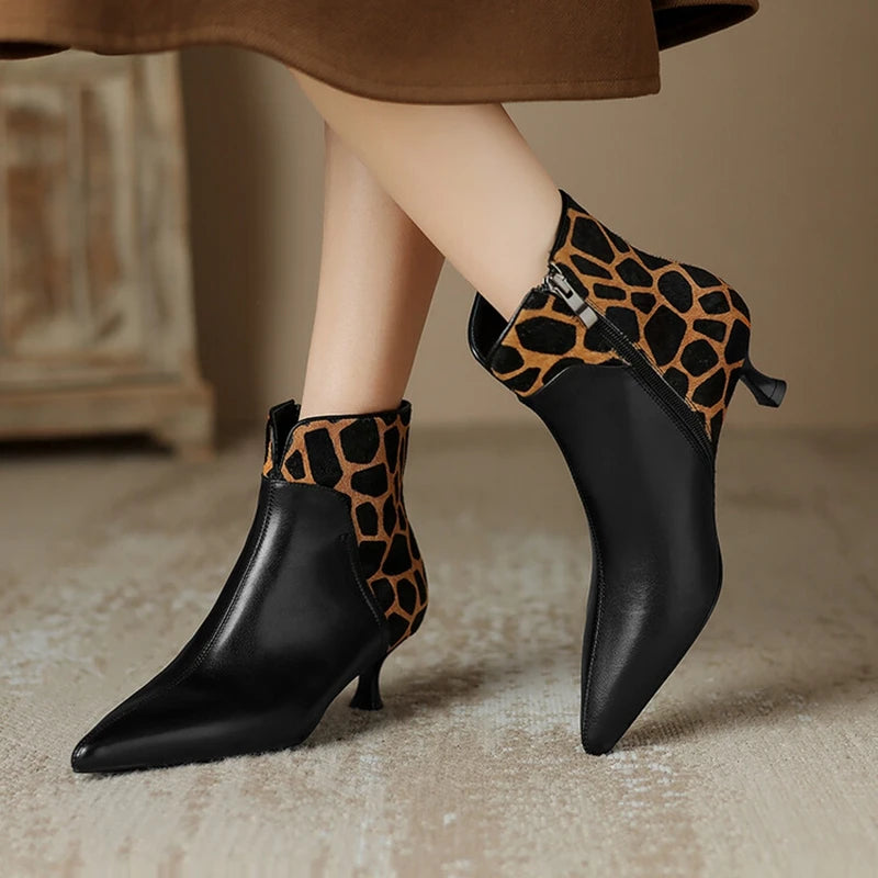 Black ankle boots with leopard print trim worn by a person on a neutral background