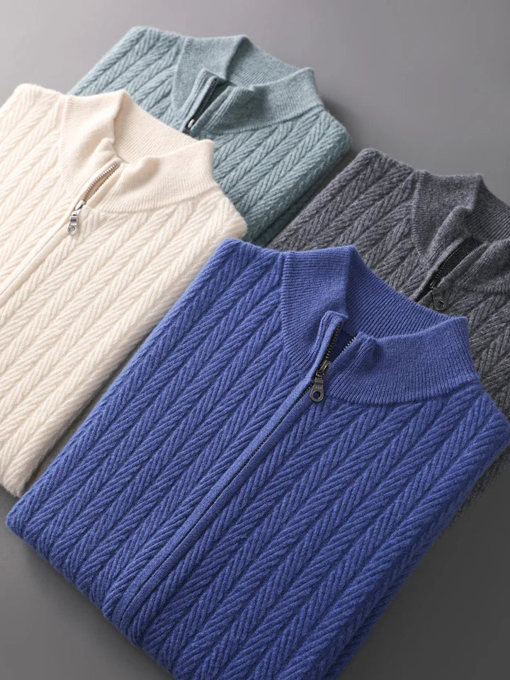 Four folded cable knit sweaters in blue, gray, and white on a gray background