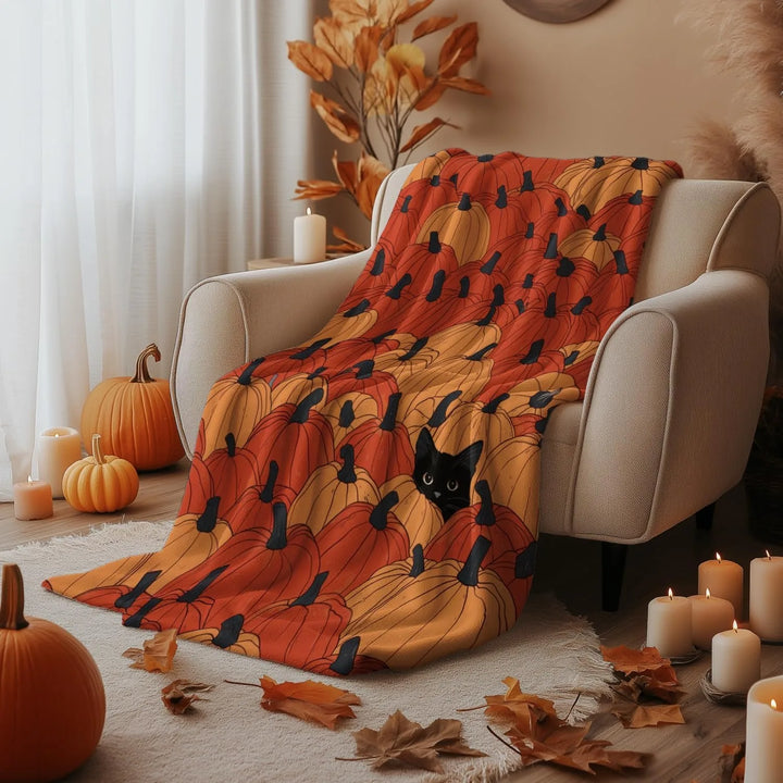 Decorative blanket with pumpkin pattern draped over a chair in a cozy room with pumpkins and candles.