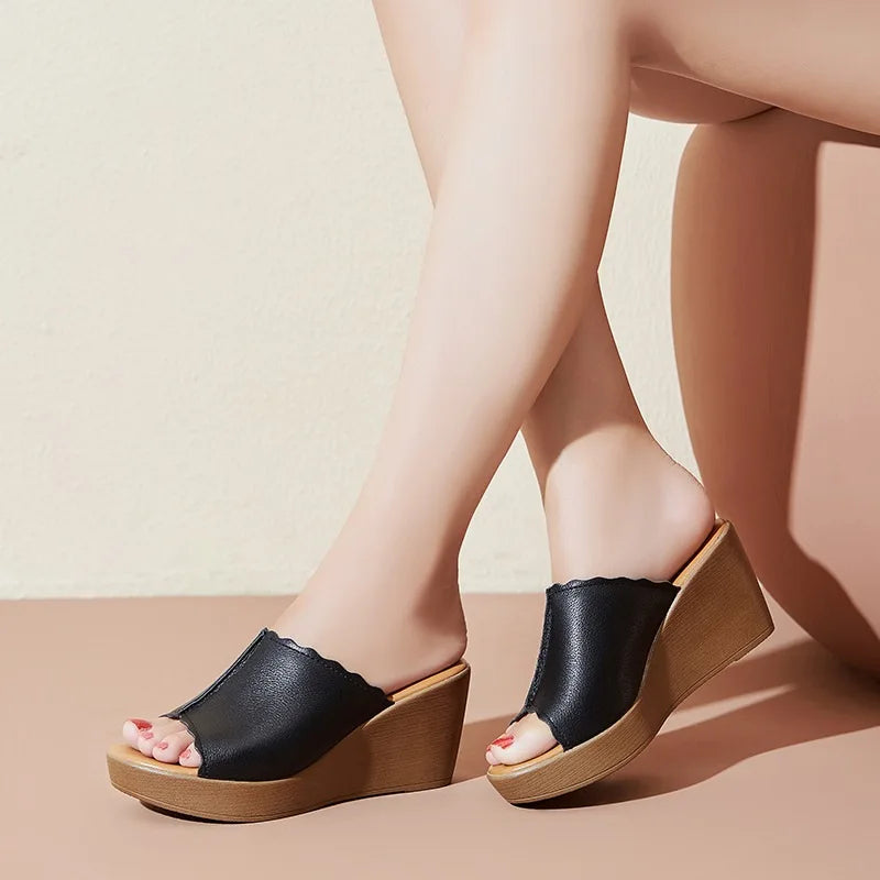 Black wedge sandals with wooden soles worn by a person on a beige background