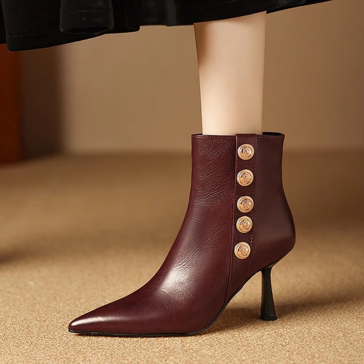 Brown leather ankle boot with gold buttons on a beige background