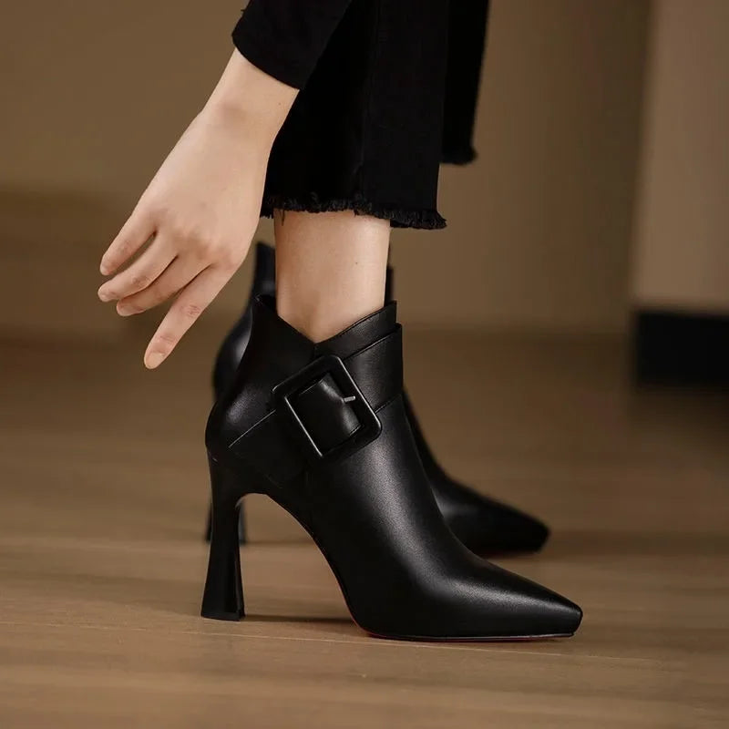 Black high-heeled boots with a buckle on a wooden floor.
