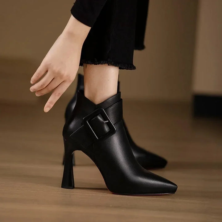 Black high-heeled boots with a buckle on a wooden floor.
