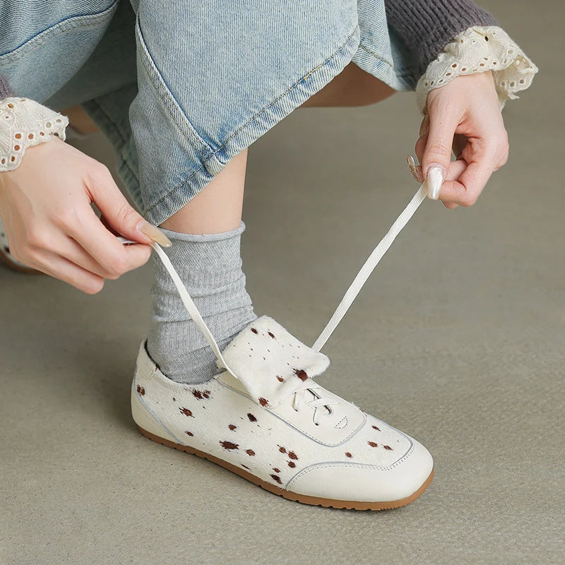 Person tying a white shoe with brown speckles on a neutral background