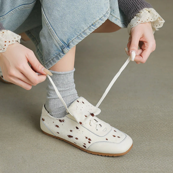 Person tying a white shoe with brown speckles on a neutral background
